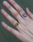 Hand wearing a gold ring with a green gemstone on a blurred background