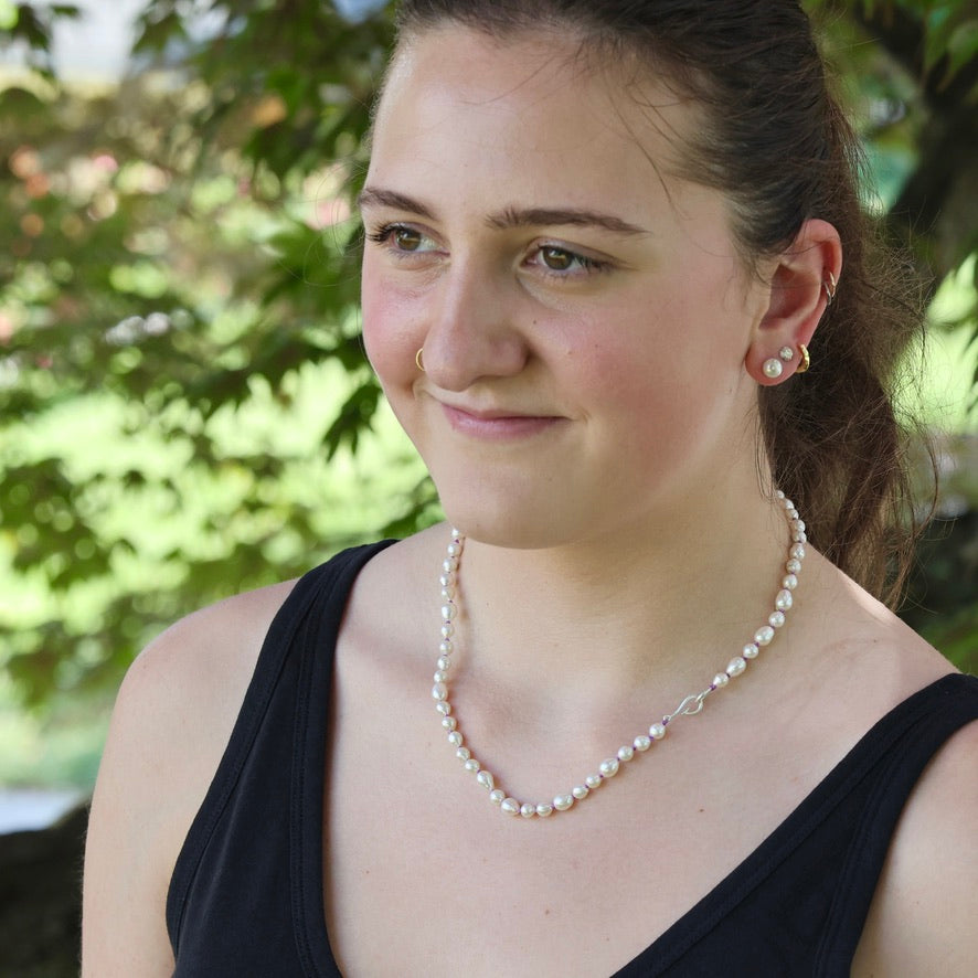 Woman wearing a pearl necklace and earrings outdoors with greenery in the background