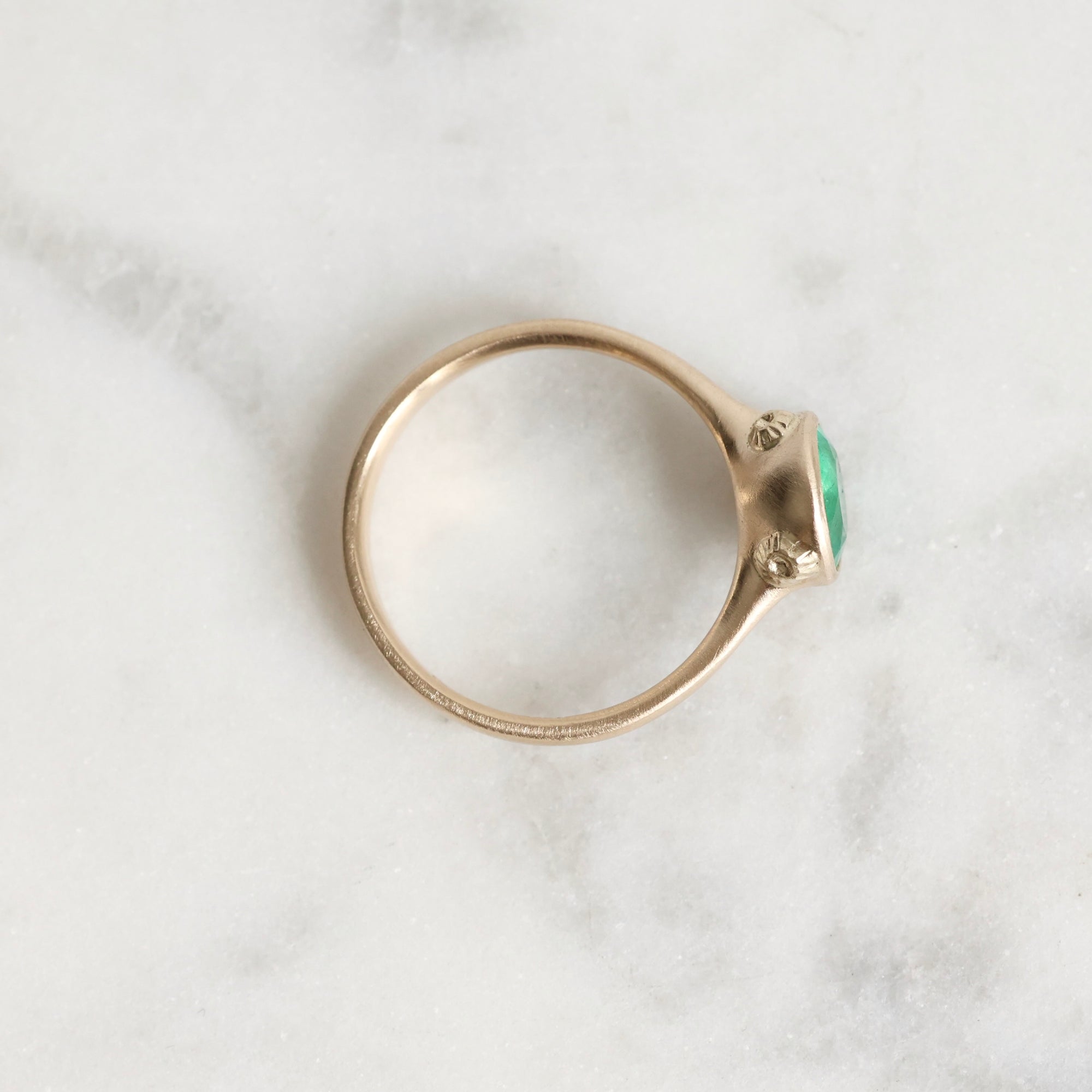 Gold ring with a green gemstone on a marble surface
