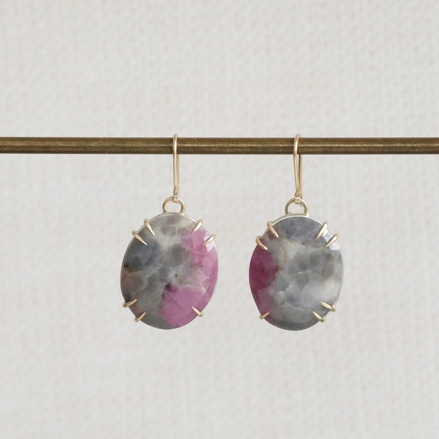 Pair of earrings with purple gemstones on a thin rod against a light gray background