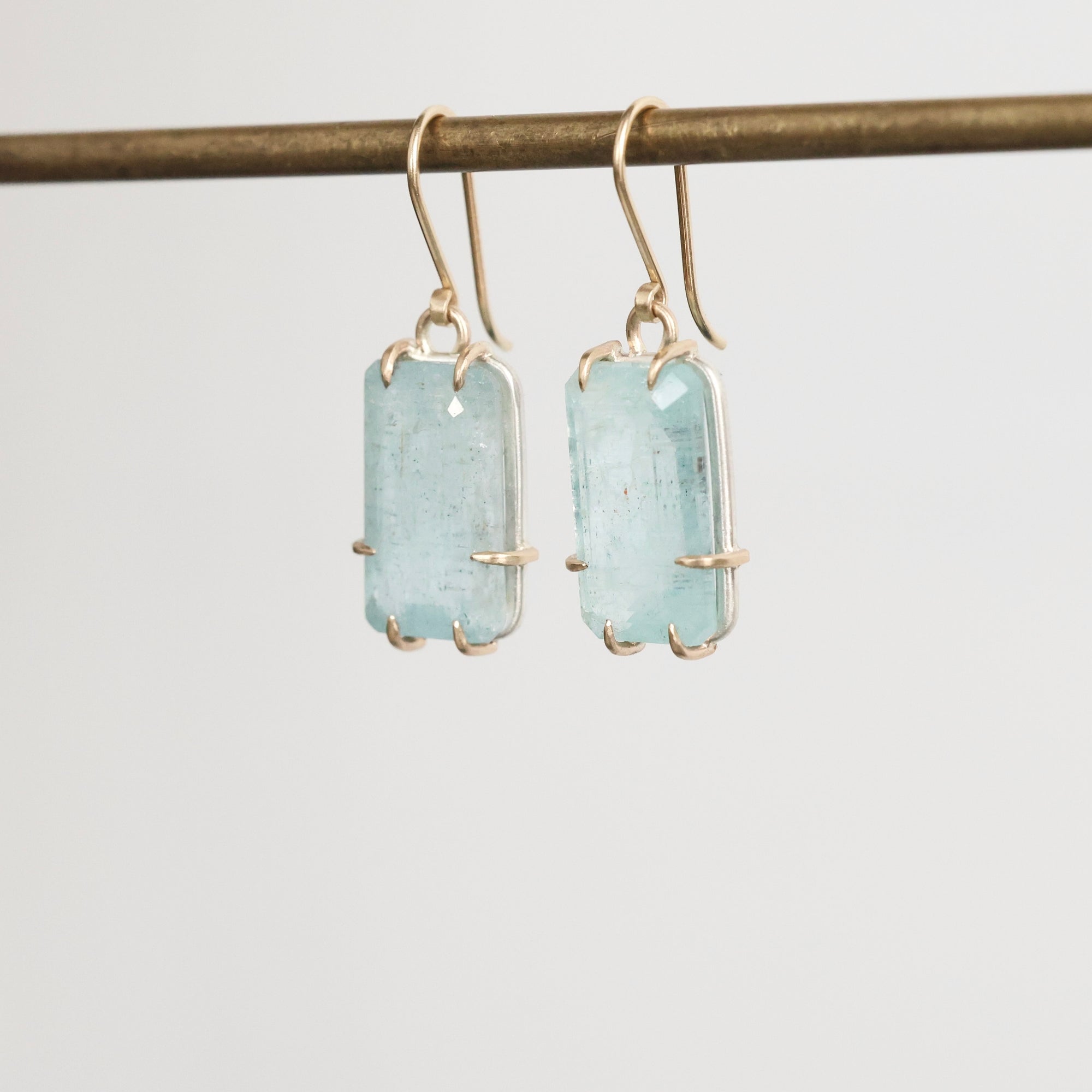 Pair of earrings with light blue gemstones on a thin rod against a white background