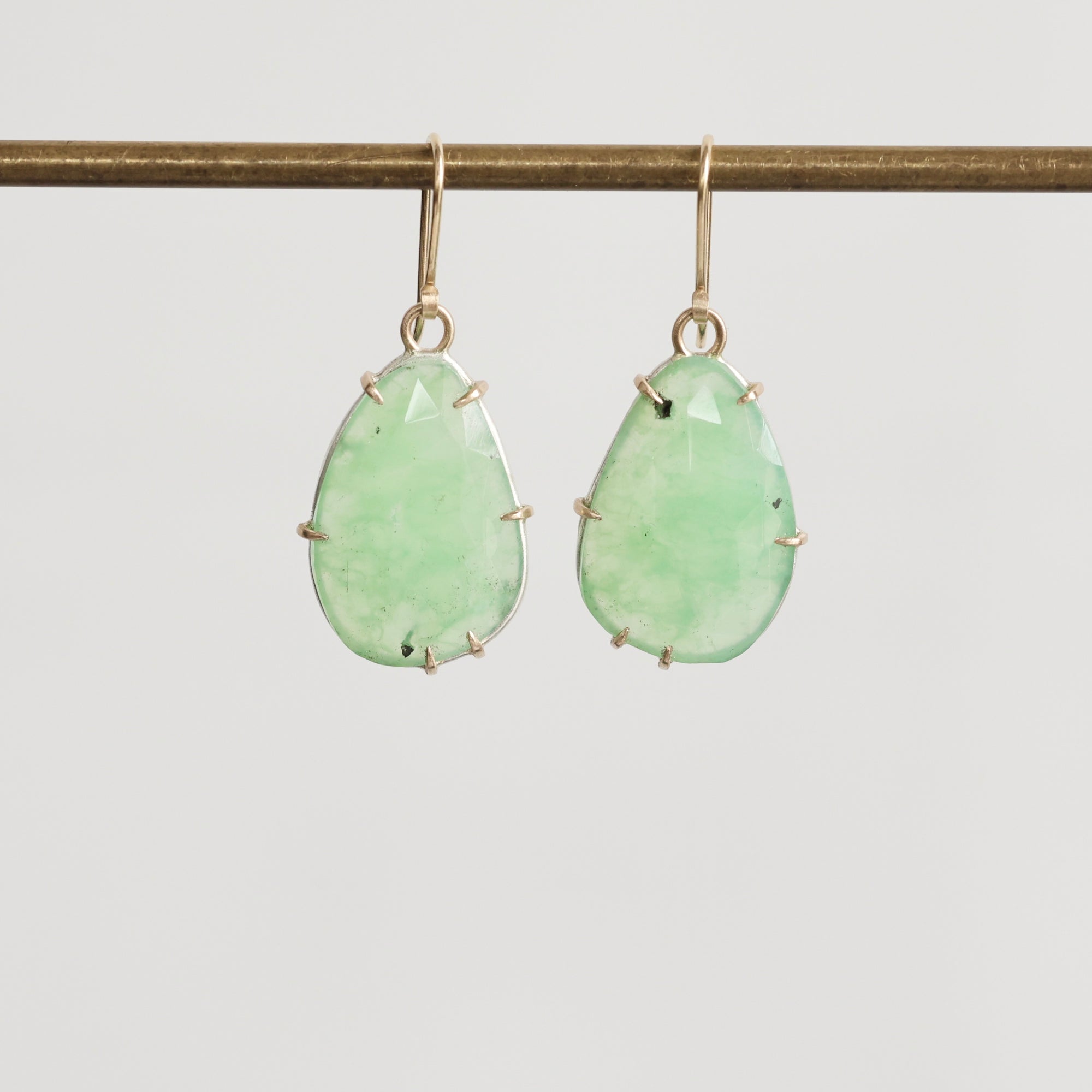 Pair of green teardrop earrings on a thin rod against a light gray background