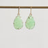Pair of green teardrop earrings on a thin rod against a light gray background