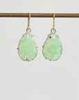 Pair of green teardrop earrings on a thin rod against a light gray background
