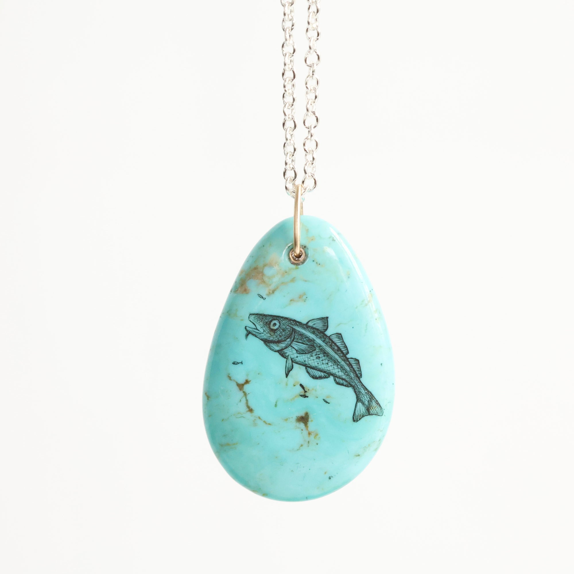Turquoise pendant with fish design on a white background