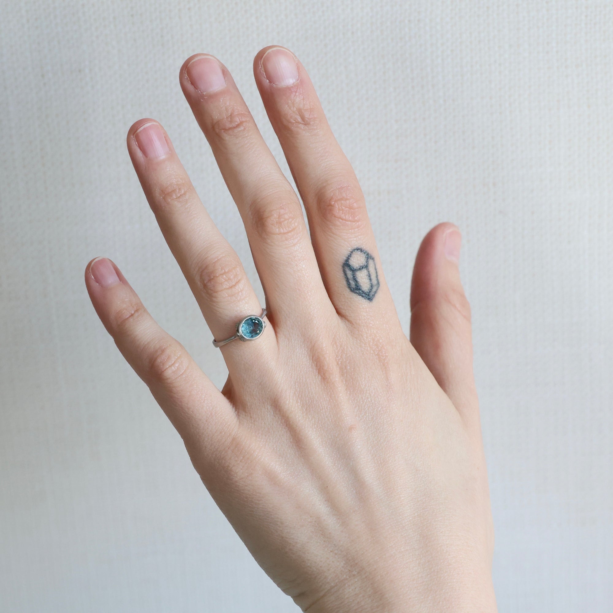 Hand wearing a ring with a blue gemstone on a neutral background