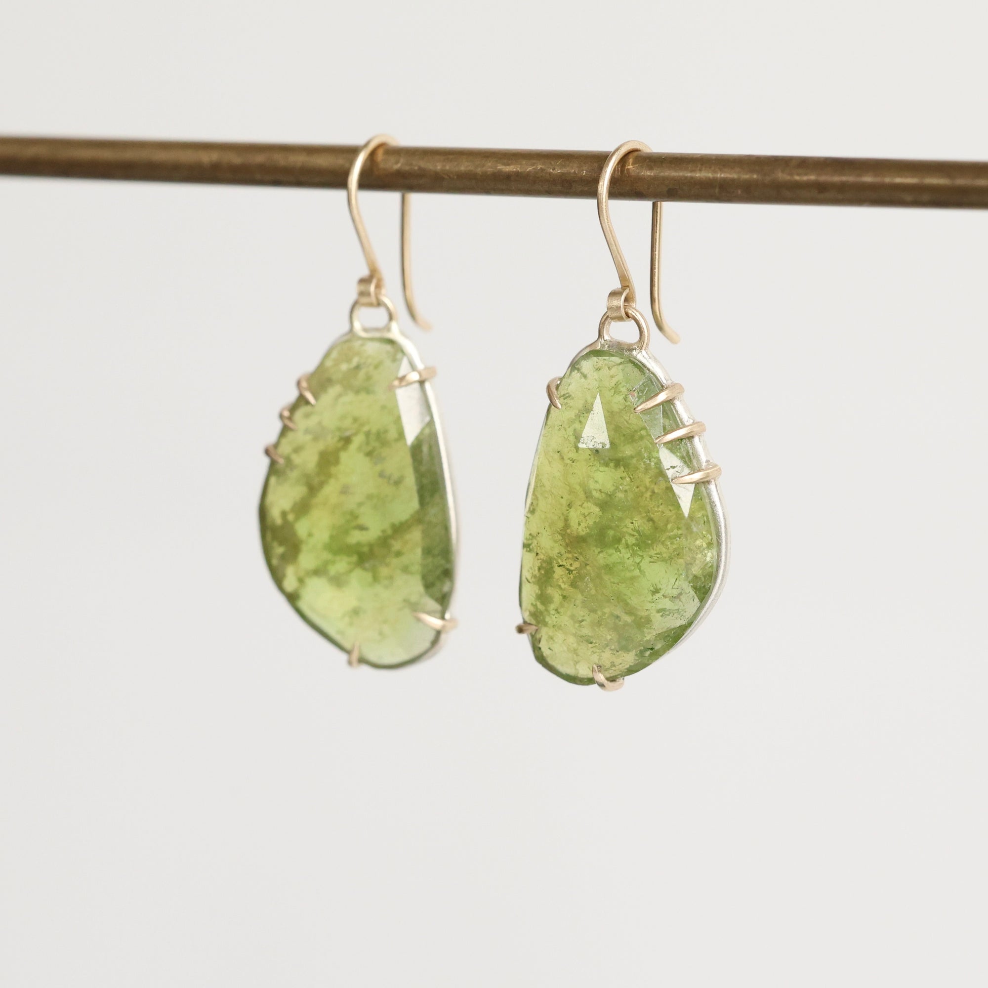 Green teardrop earrings on a thin rod against a light gray background