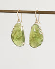 Green teardrop earrings on a thin rod against a light gray background