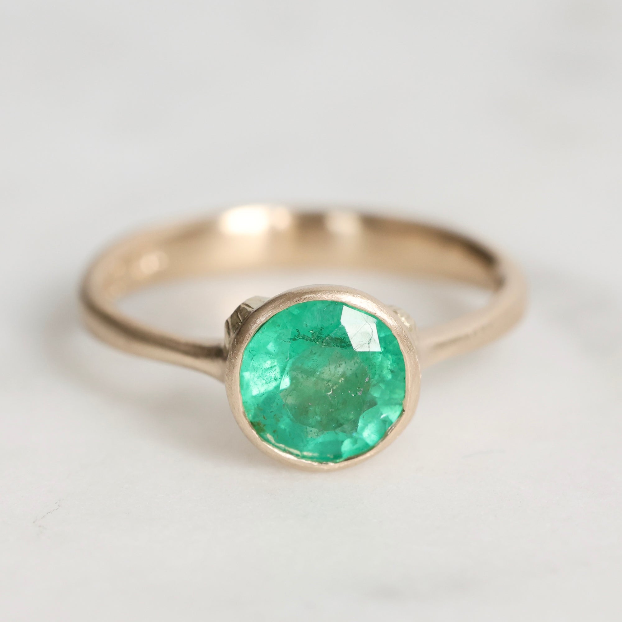 Gold ring with a green gemstone on a light gray background