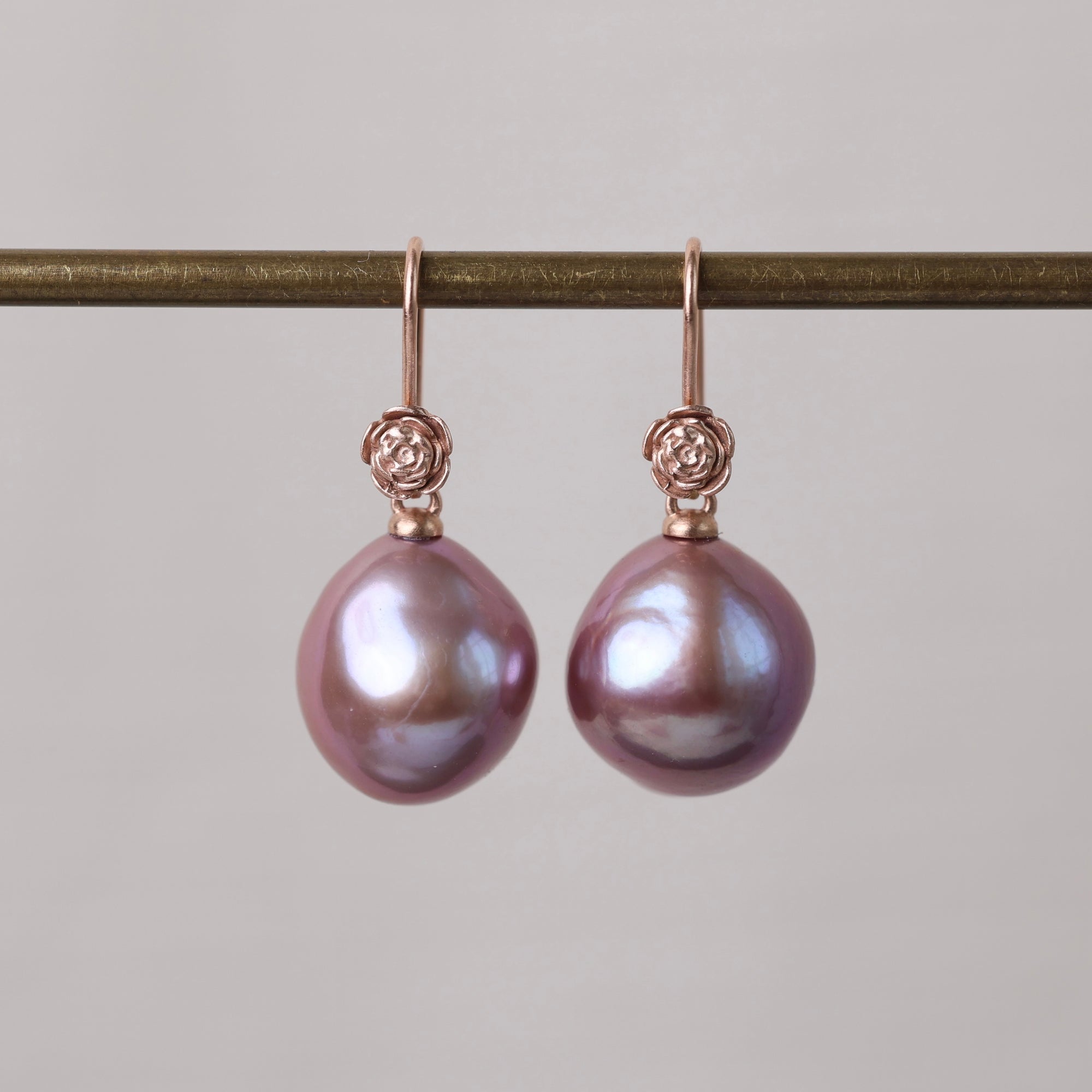Pair of pink pearl earrings on a gold hook against a gray background