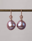 Pair of pink pearl earrings on a gold hook against a gray background