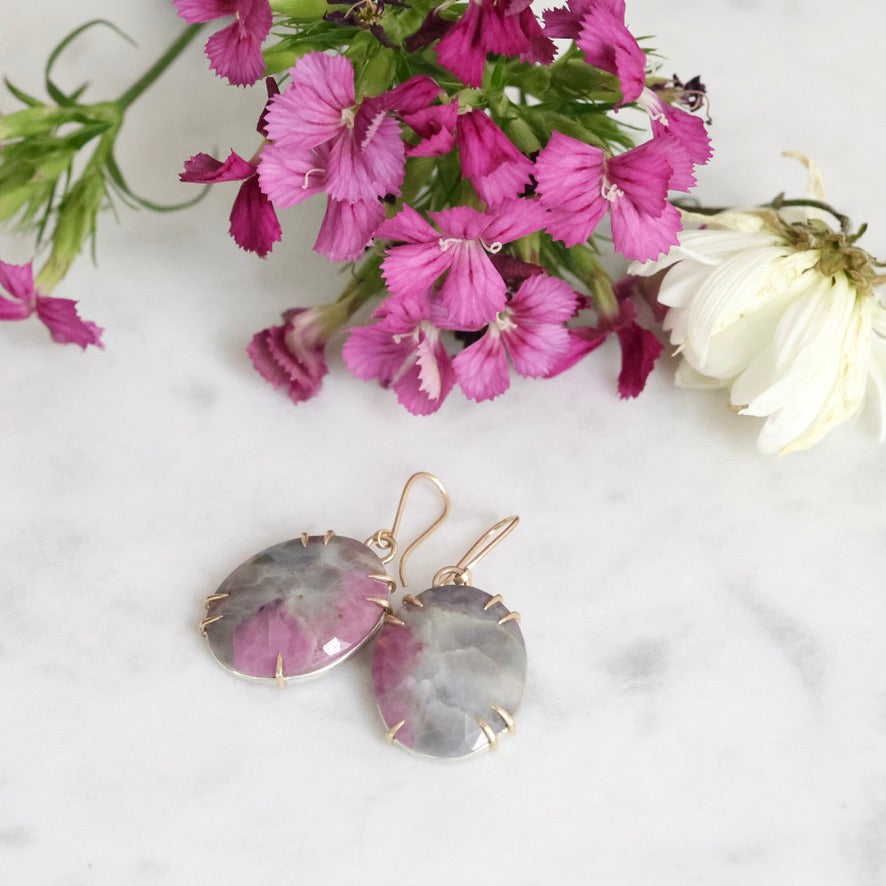 Earrings with pink and gray stones on a marble surface with flowers.