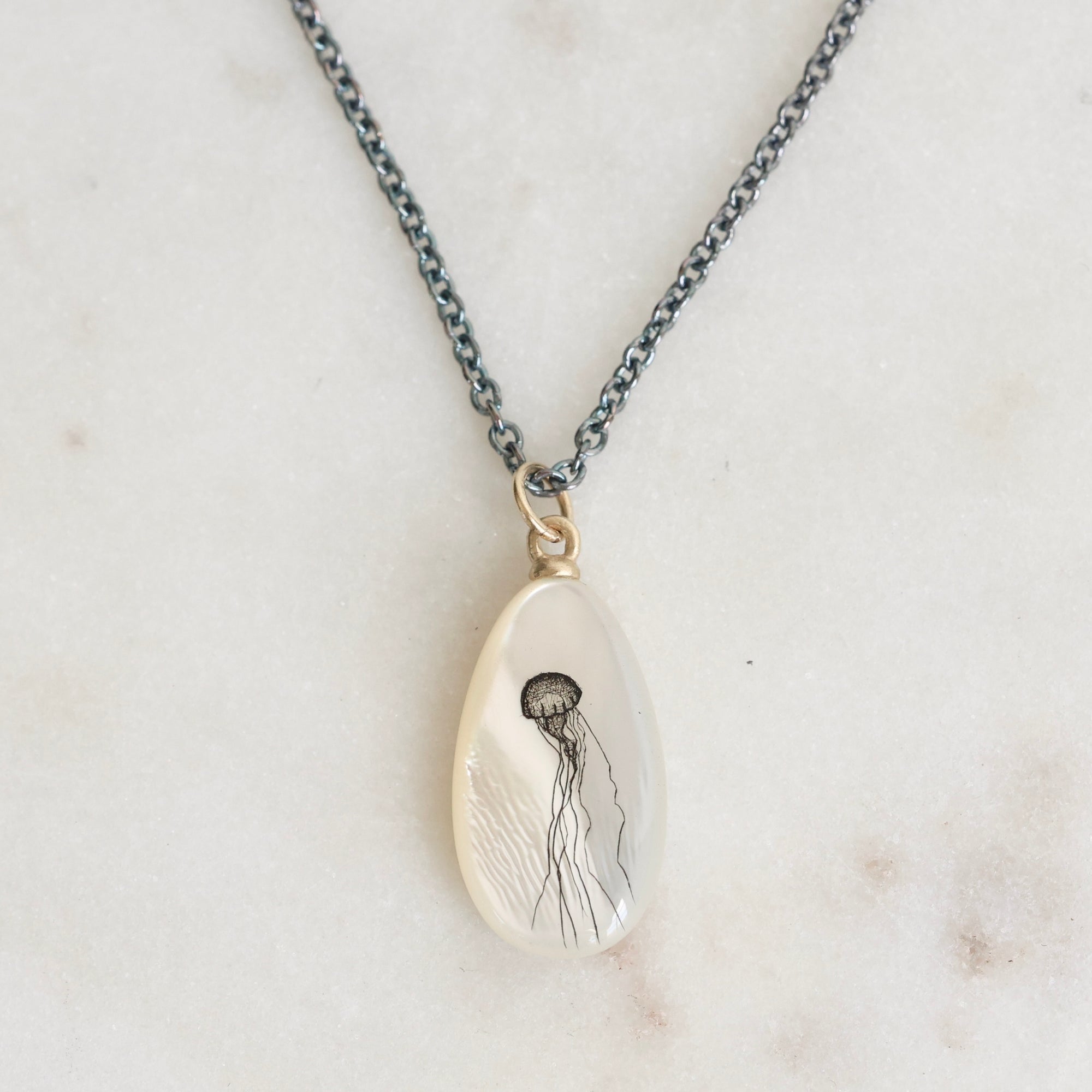 Teardrop-shaped pendant with jellyfish design on a chain against a marble background
