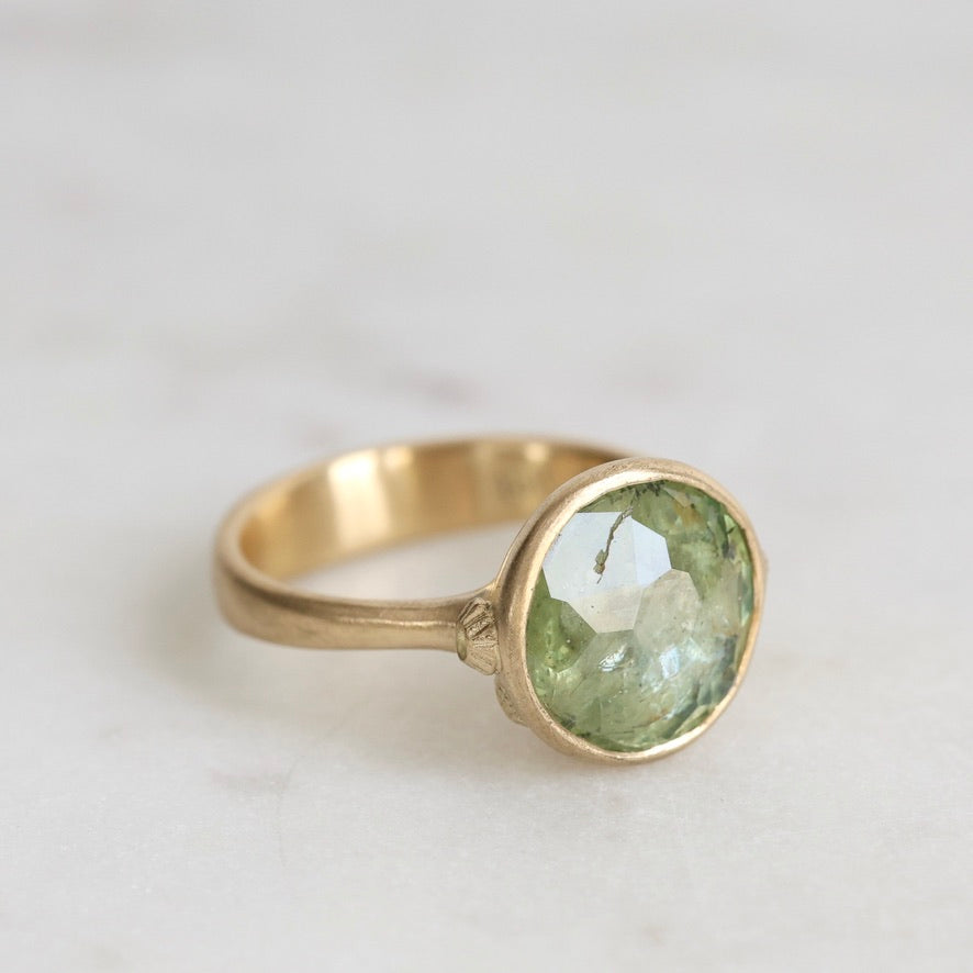 Gold ring with a green gemstone on a light background