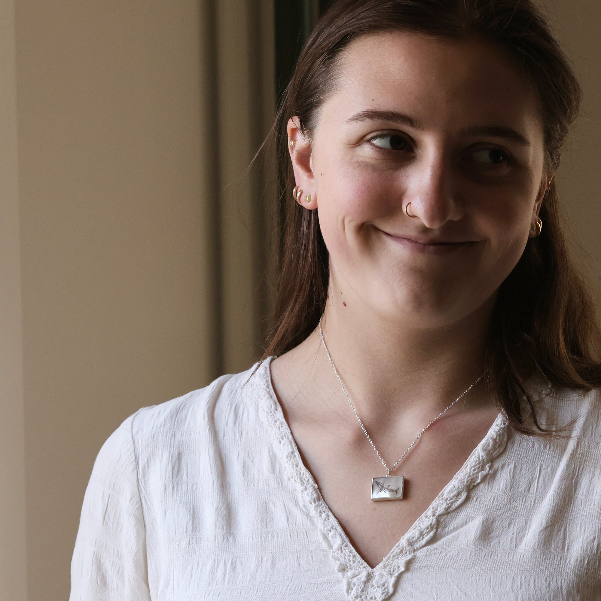 Woman wearing a white blouse with a necklace against a neutral background