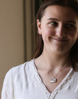Woman wearing a white blouse with a necklace against a neutral background