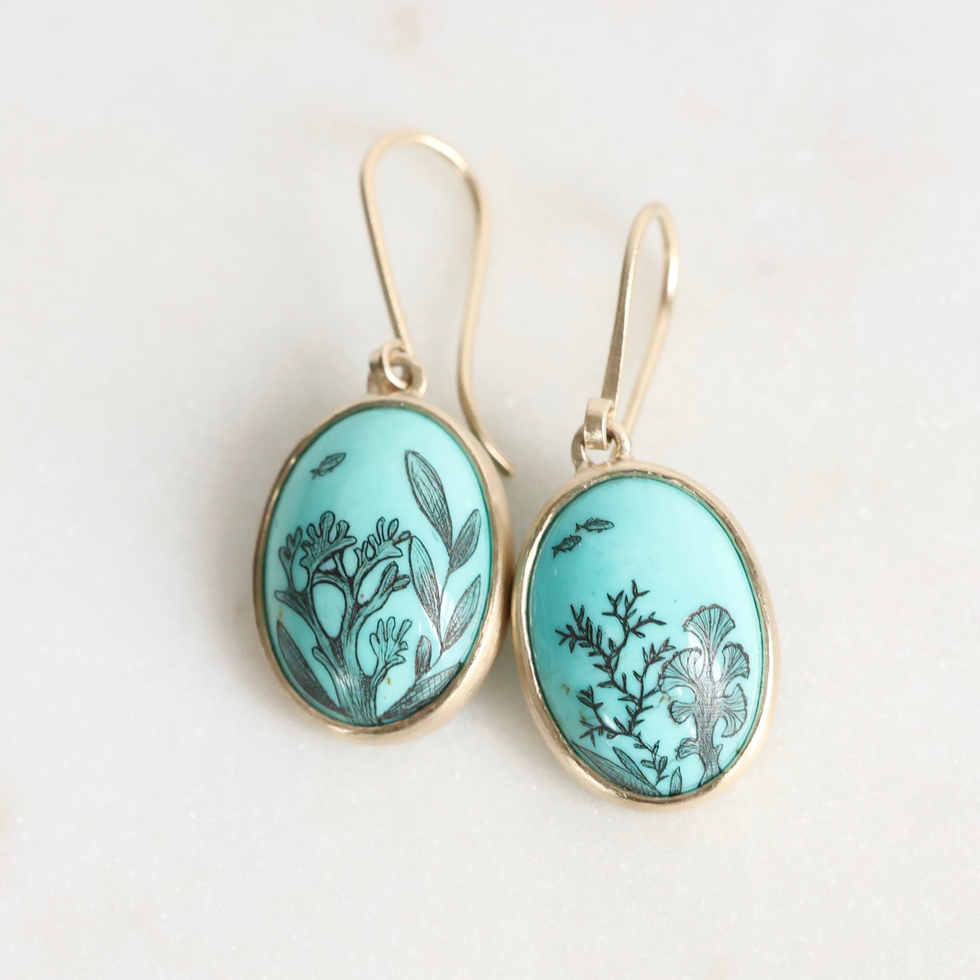 Pair of earrings with turquoise oval stones featuring black seaweed patterns on a white background