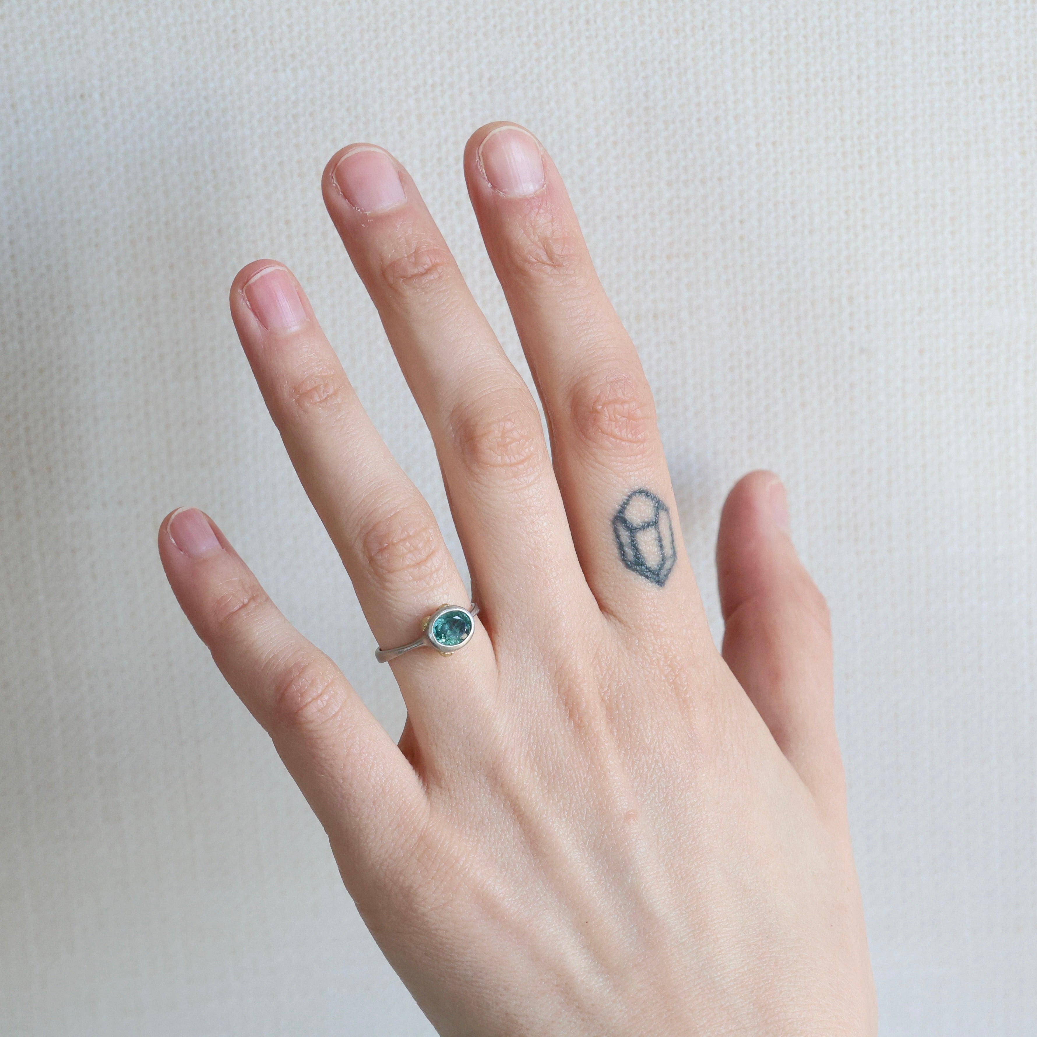 Hand wearing a ring with a blue gemstone on a plain background