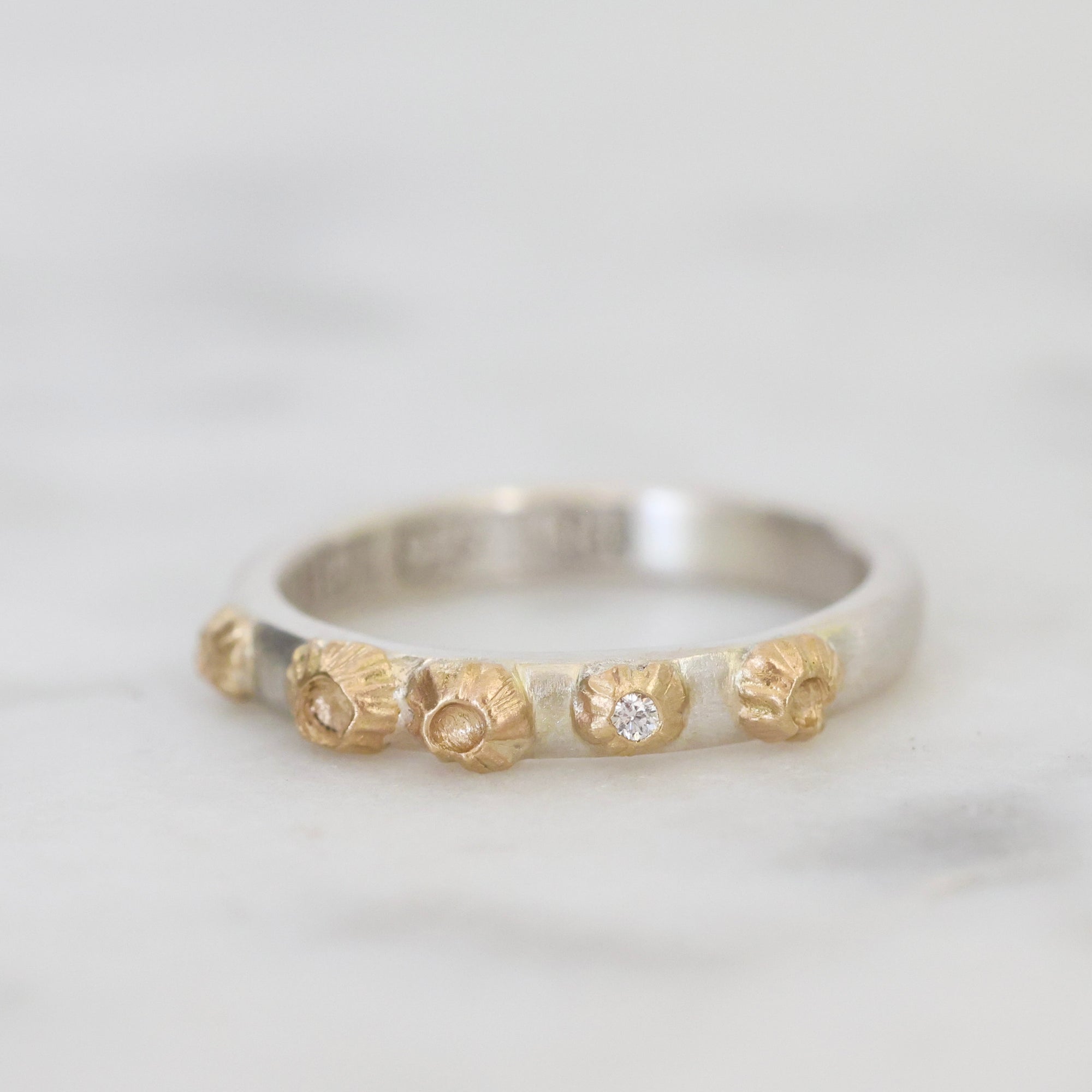 Silver ring with gold accents and a diamond on a light gray background