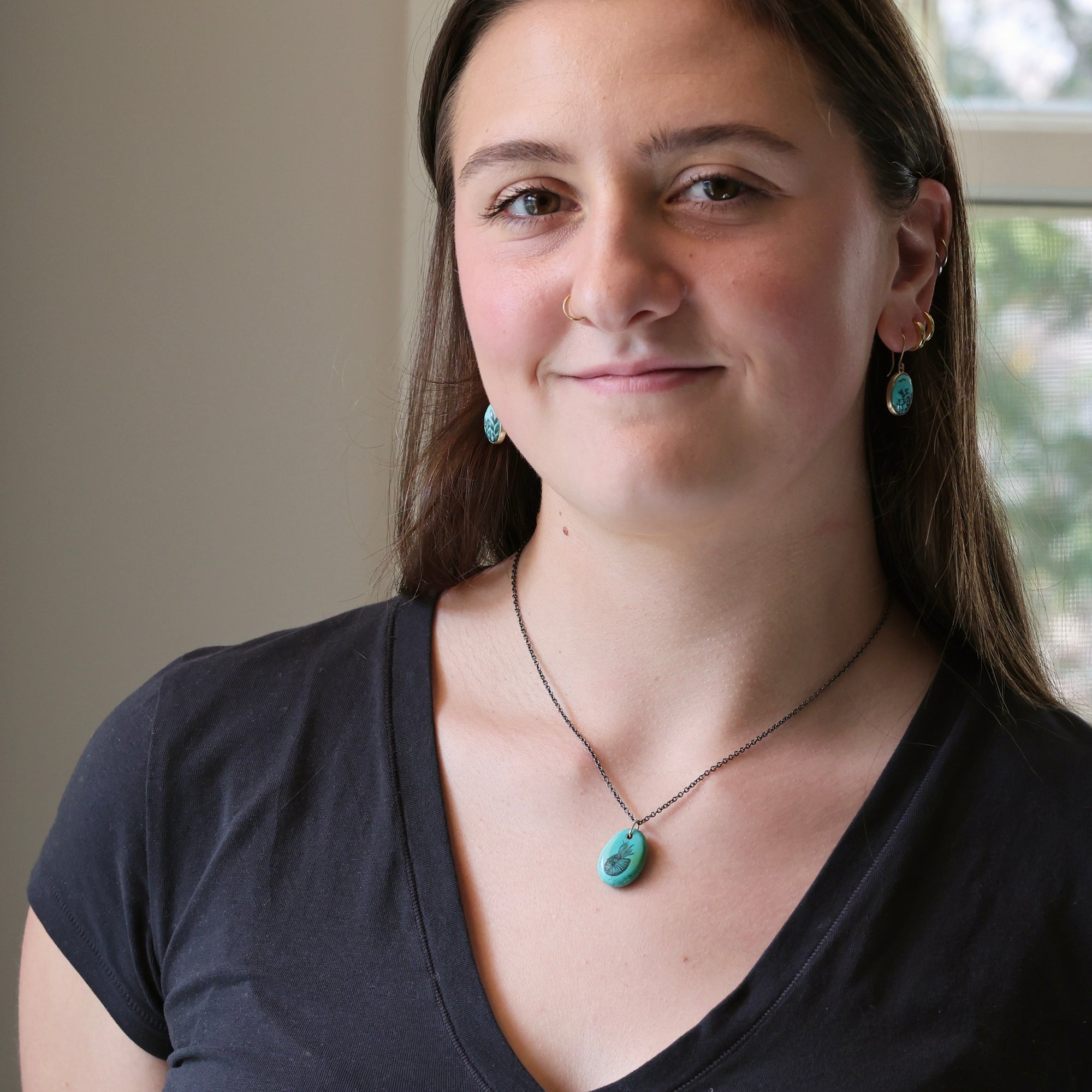 Woman wearing a black top and turquoise necklace and earrings indoors.