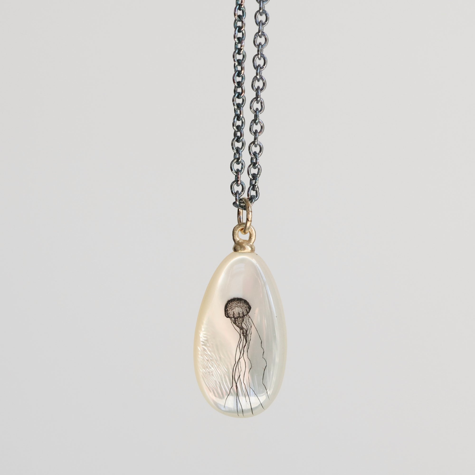 Teardrop-shaped pendant with jellyfish design on a chain against a light gray background