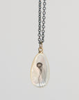Teardrop-shaped pendant with jellyfish design on a chain against a light gray background