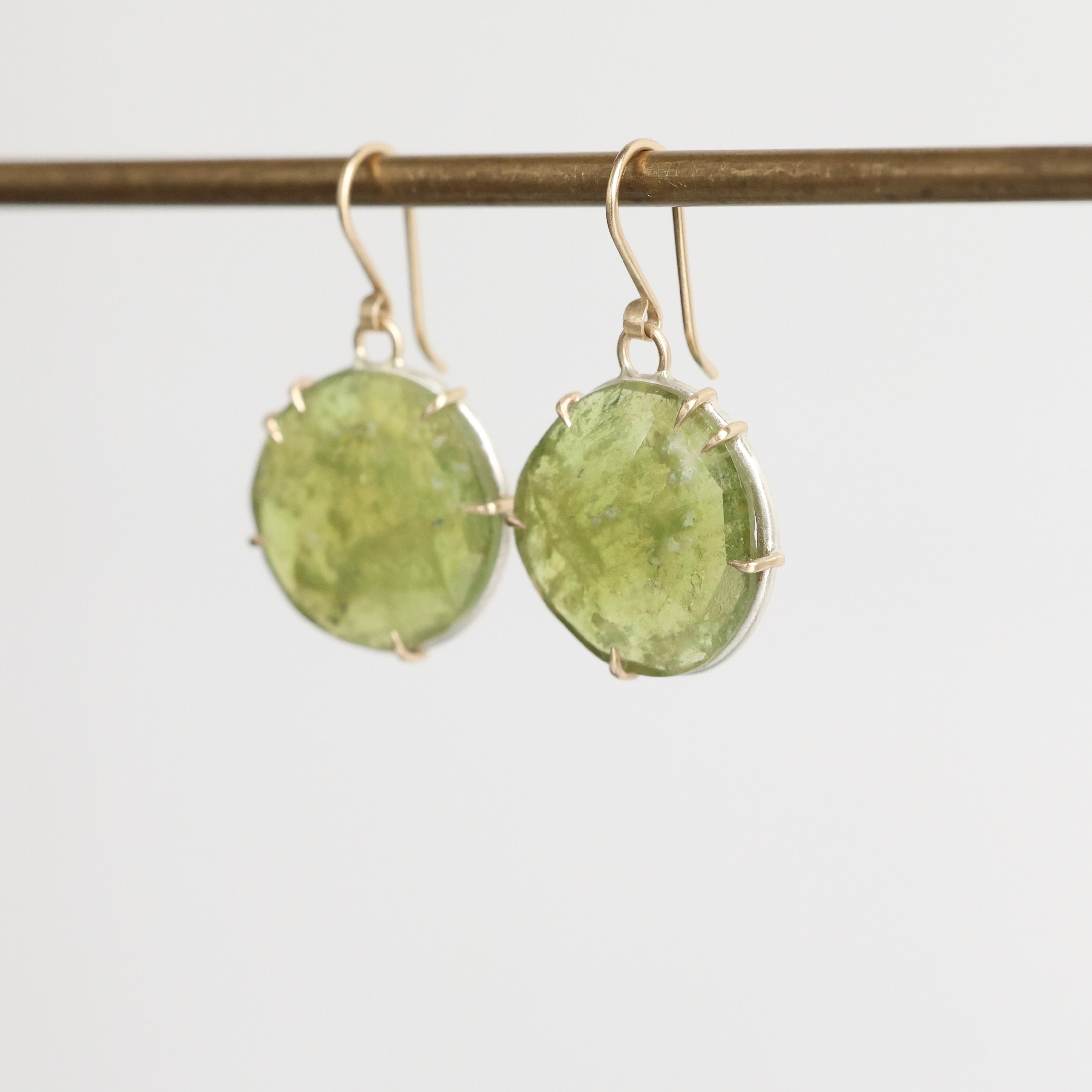 Green stone earrings on a thin rod against a light gray background