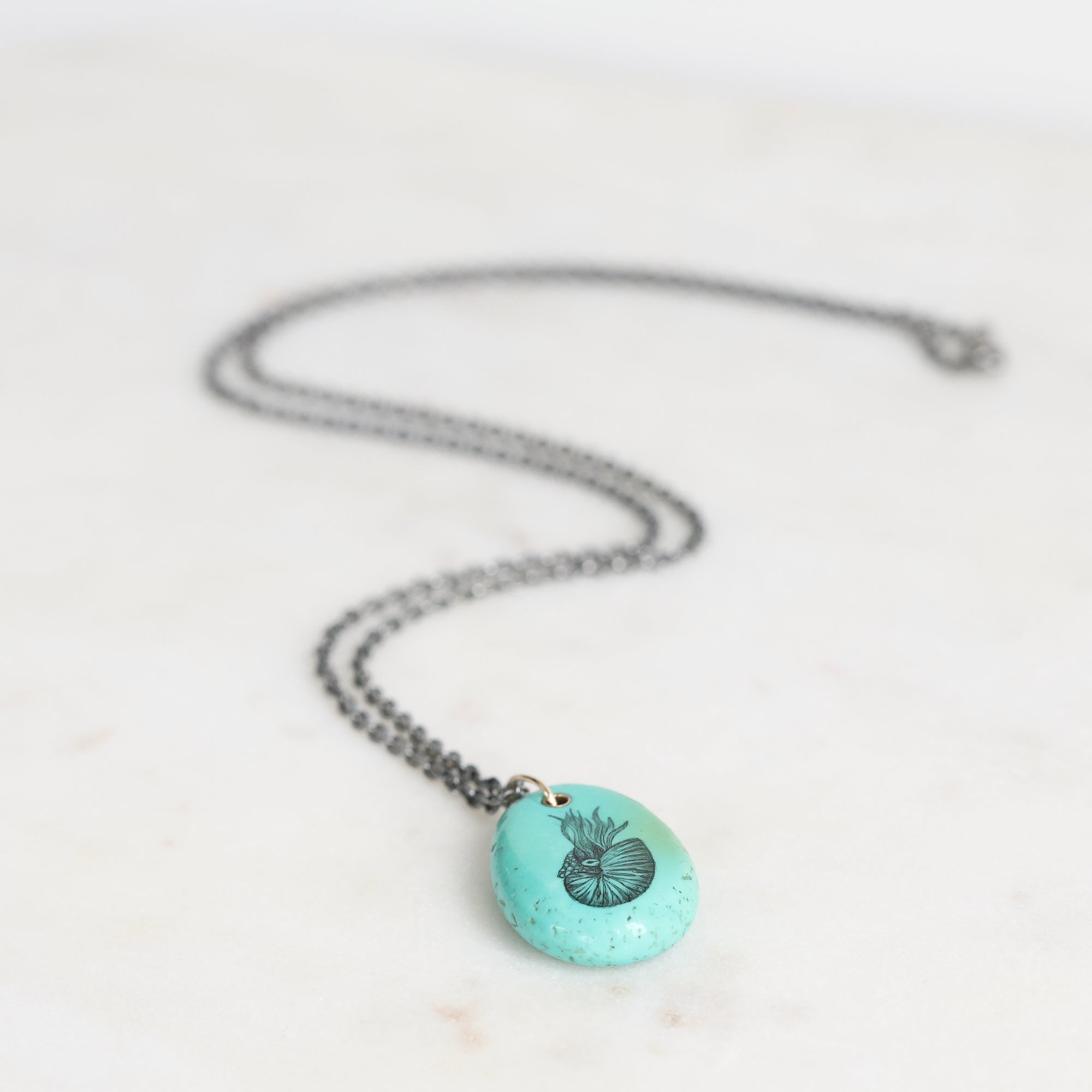 Necklace with a turquoise pendant featuring a black design on a light gray background