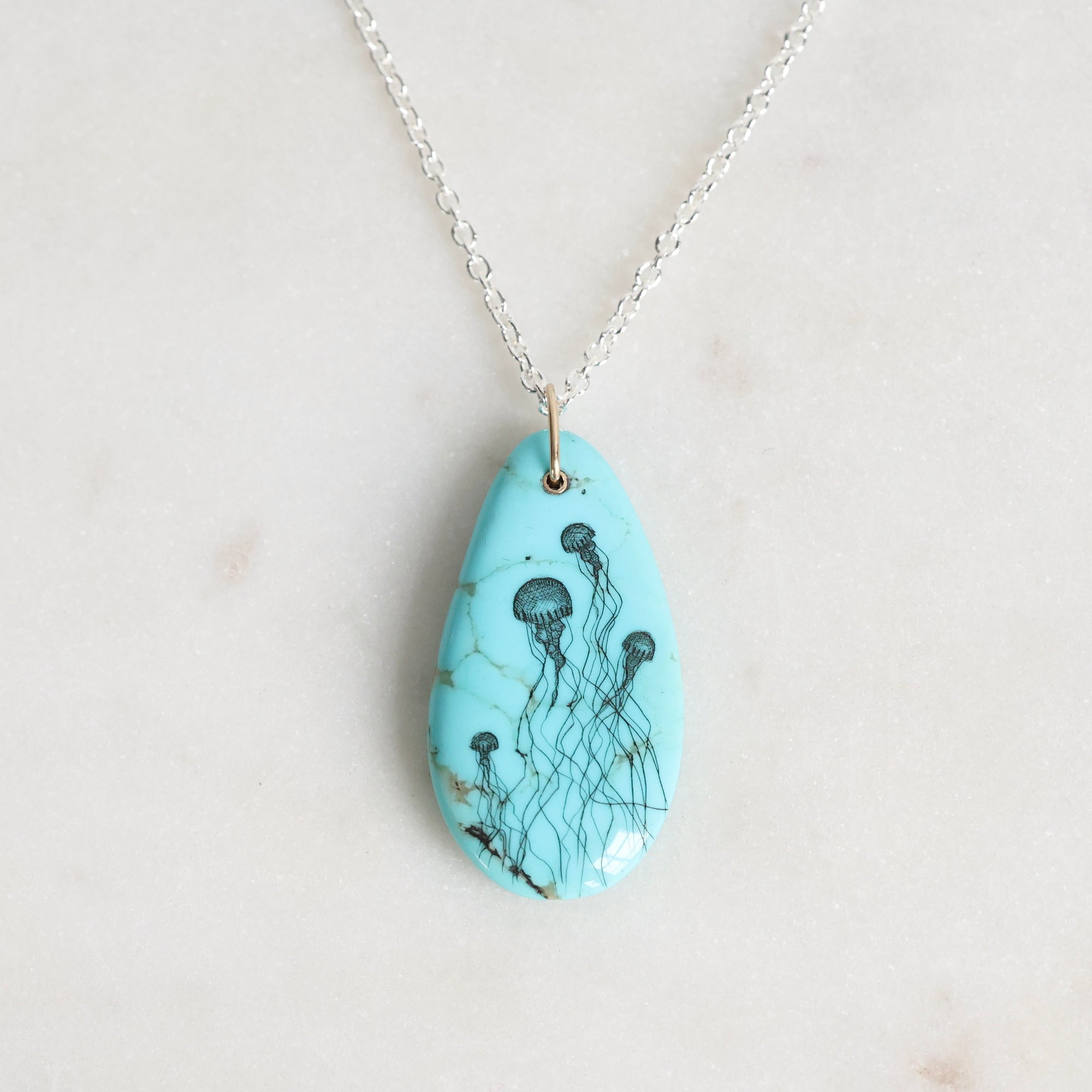Turquoise pendant with jellyfish design on a silver chain against a light gray background