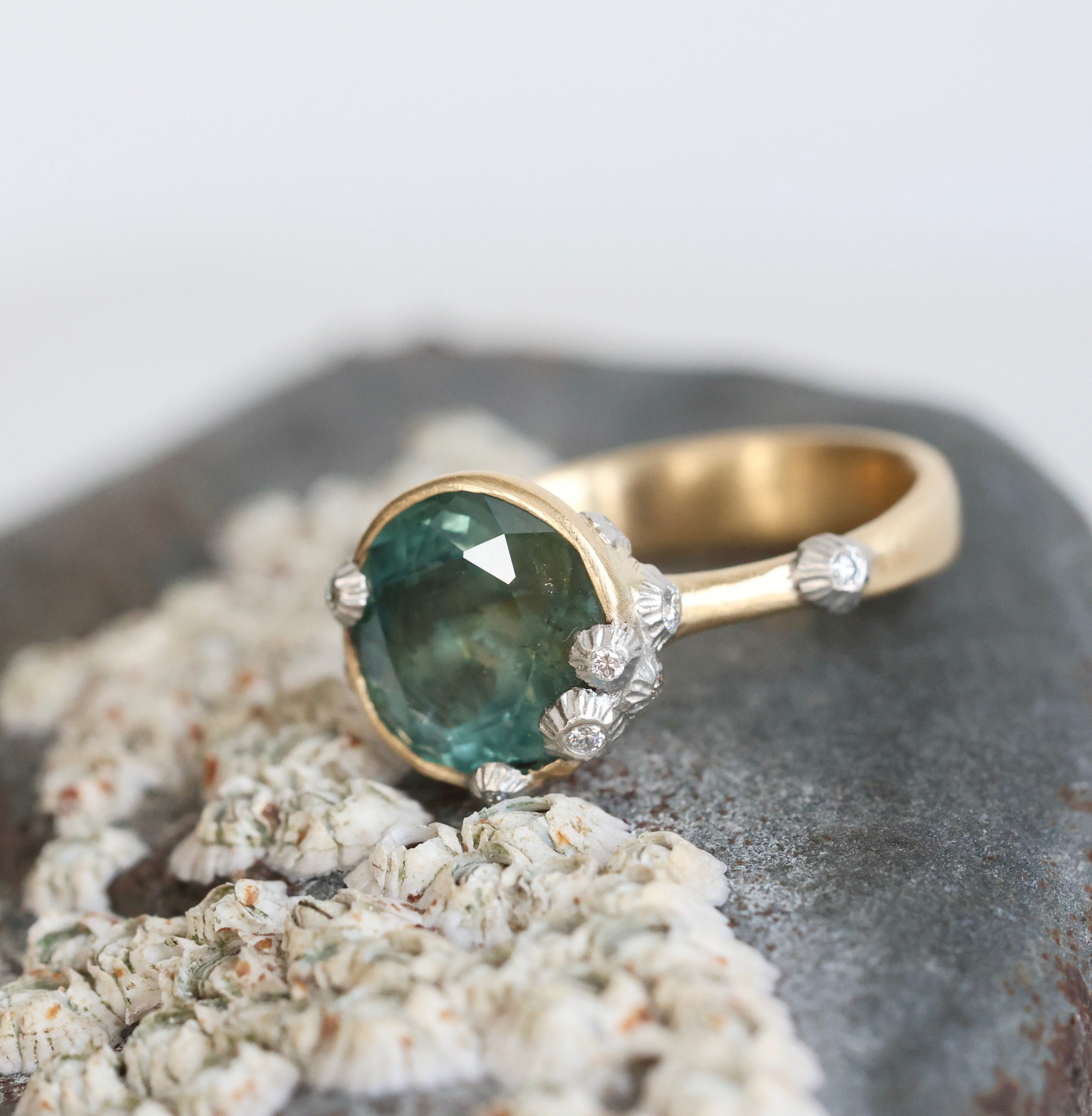 Large green sapphire ring with lots of barnacles on top of a barnacle full rock. Gold shank