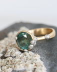 Large green sapphire ring with lots of barnacles on top of a barnacle full rock. Gold shank