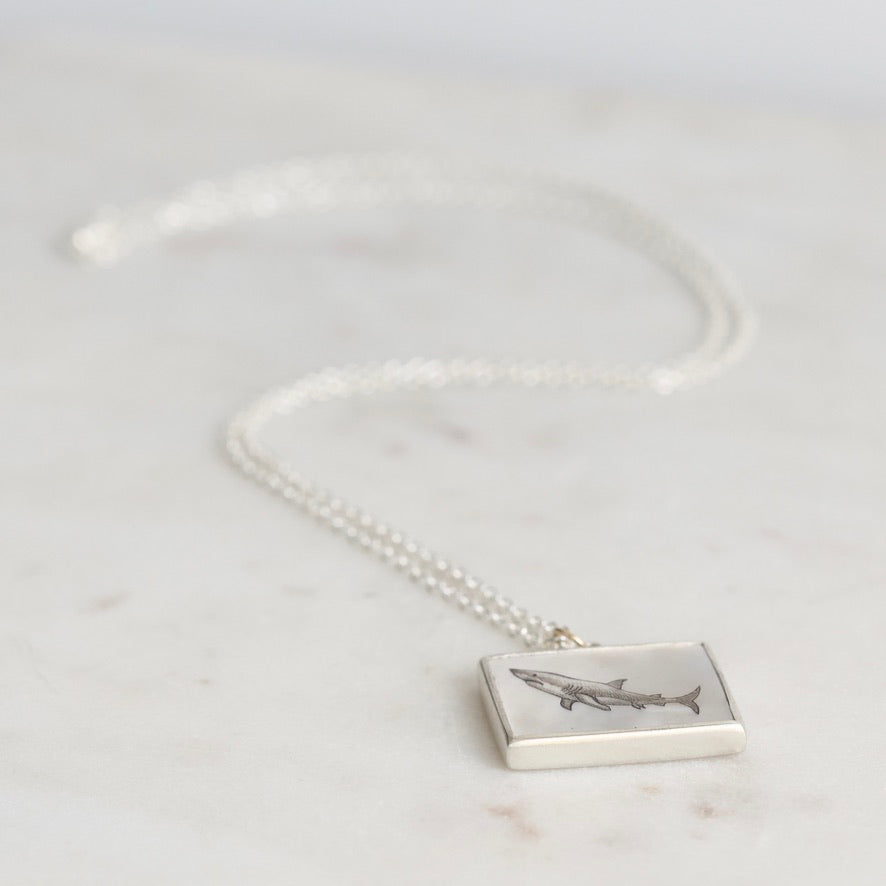 Silver necklace with a rectangular pendant featuring an engraved design on a light gray background