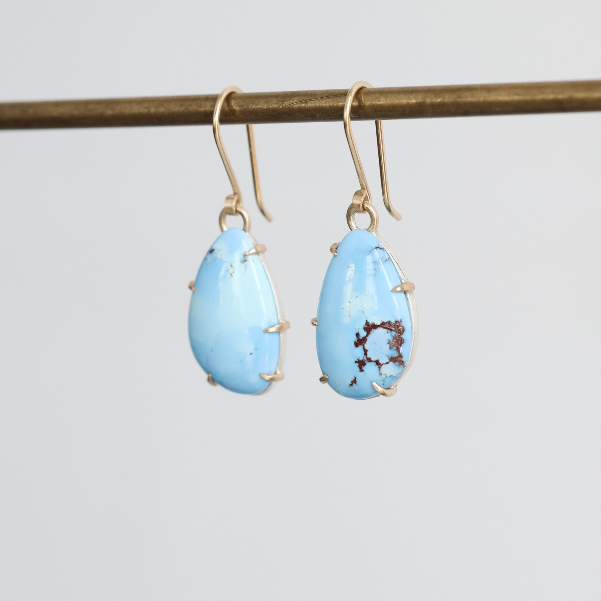 Pair of blue teardrop earrings on a gold earring stand against a light gray background