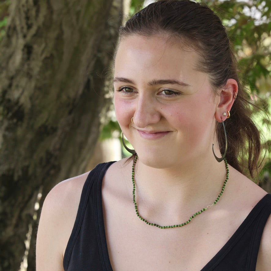 Woman wearing a black top and green necklace with trees in the background