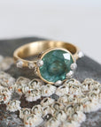 Large green sapphire ring with lots of barnacles on top of a barnacle full rock. Gold shank