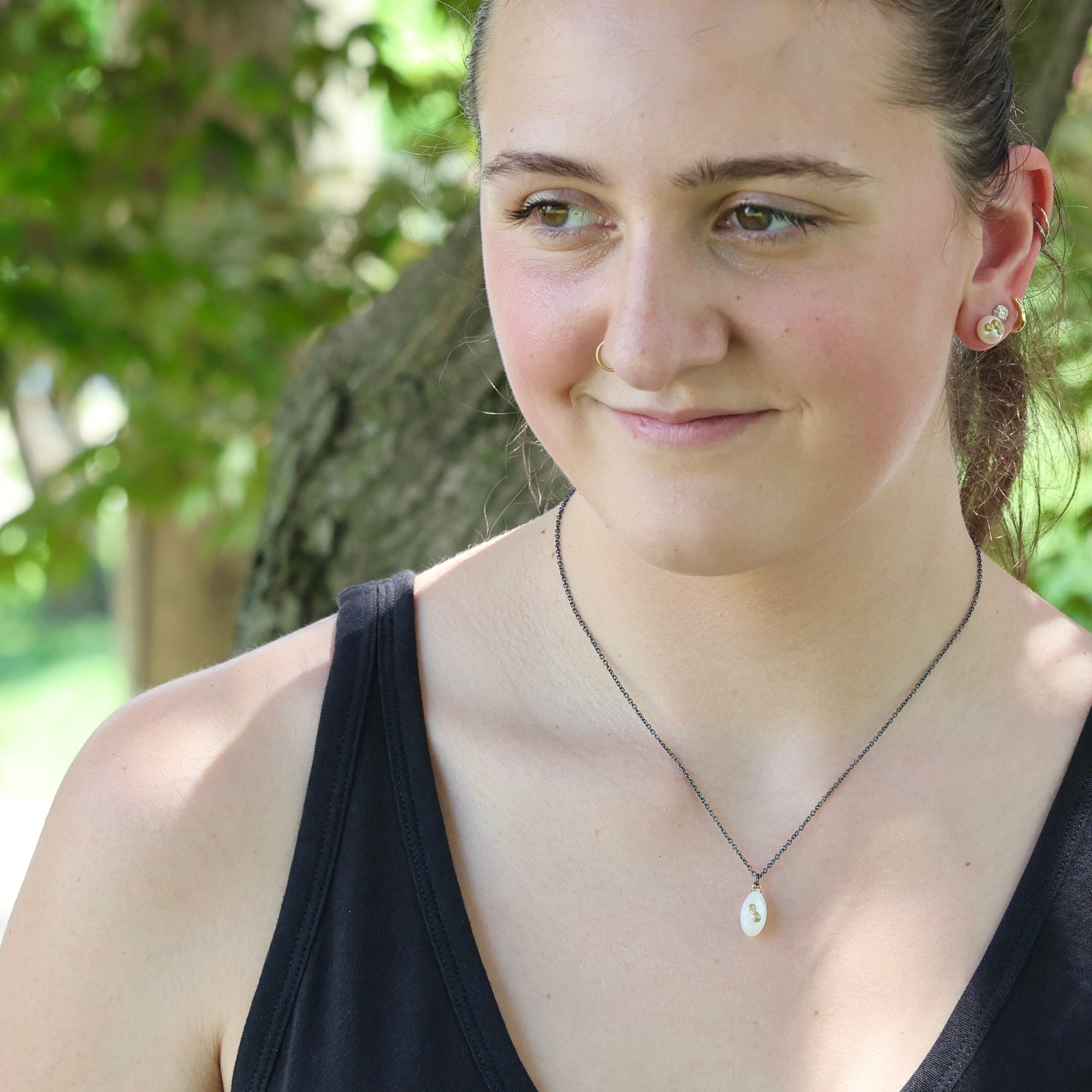 Woman wearing a black tank top and necklace with a blurred natural background