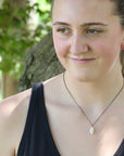 Woman wearing a black tank top and necklace with a blurred natural background
