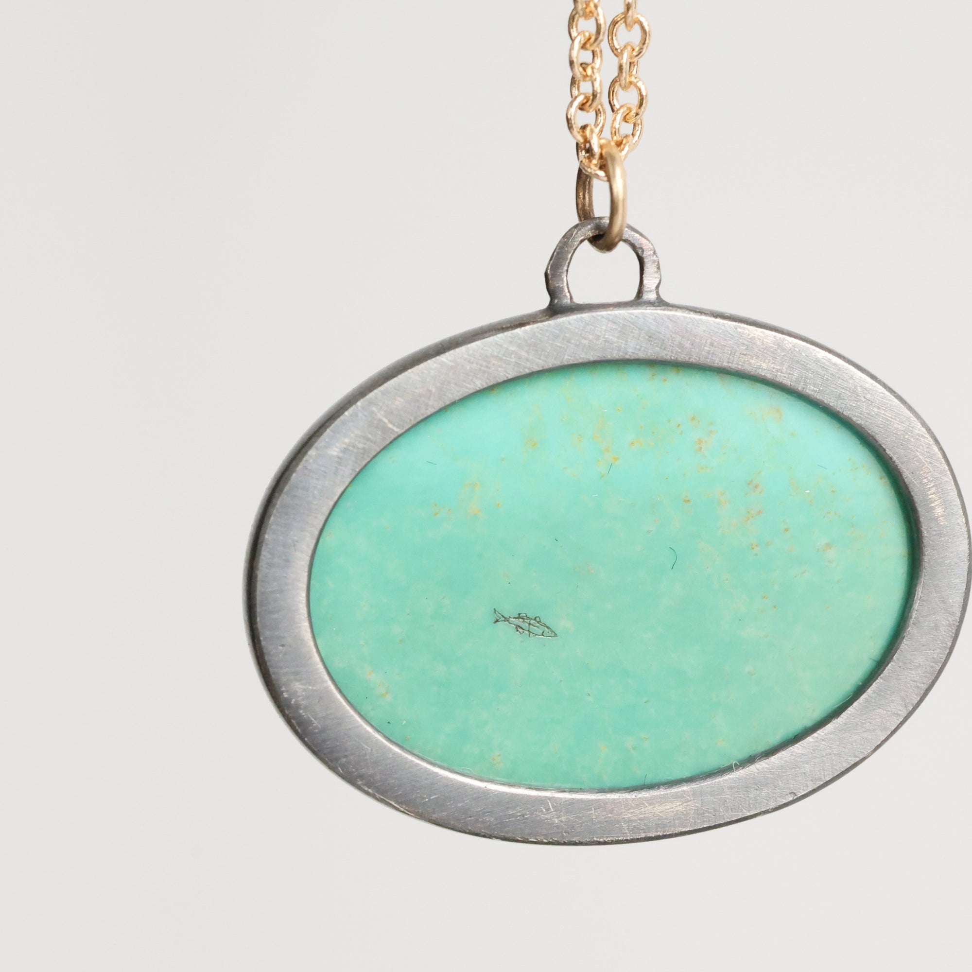 Necklace with a pendant featuring a green stone and gold accents on a light gray background