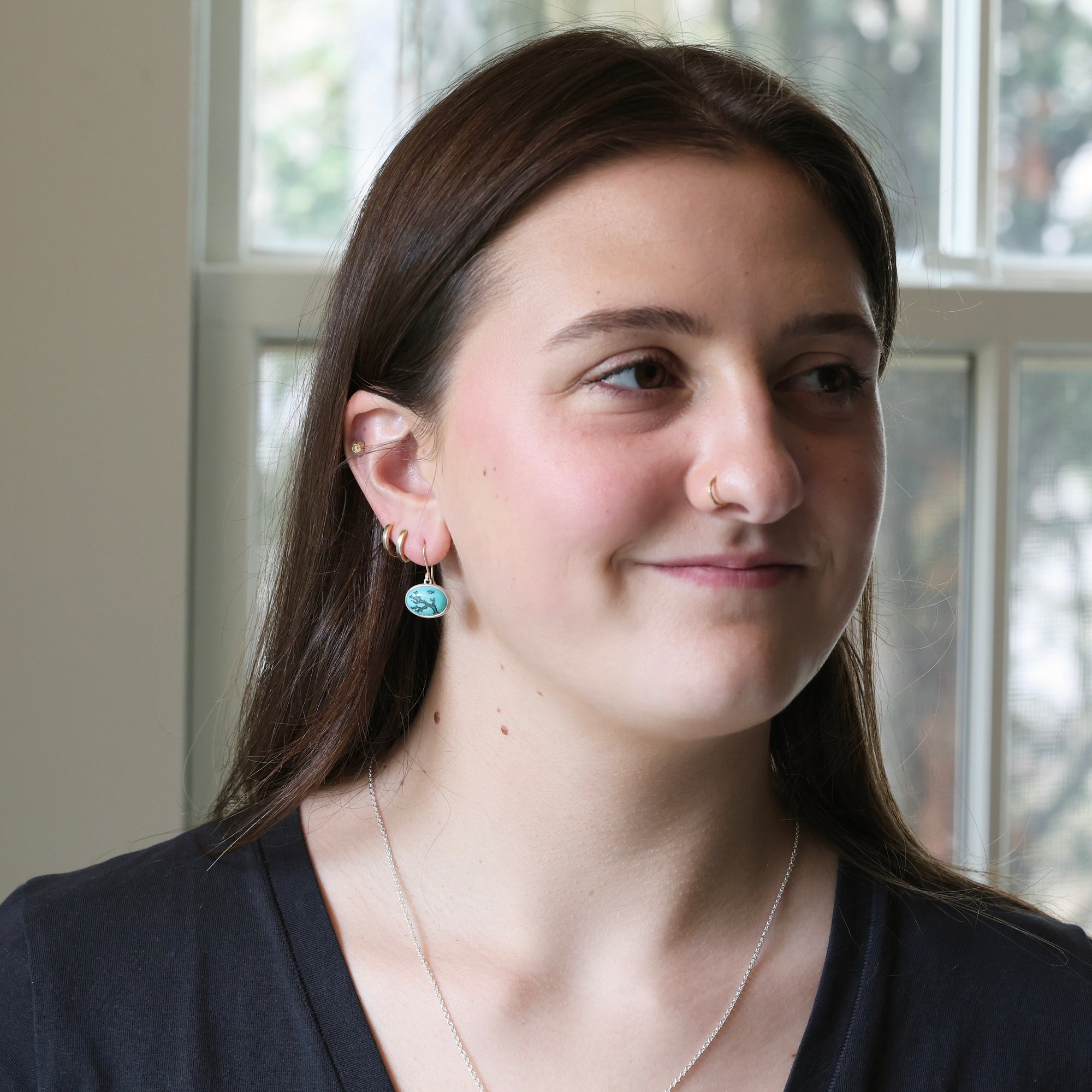 Woman wearing earrings and a necklace, standing indoors with a neutral background