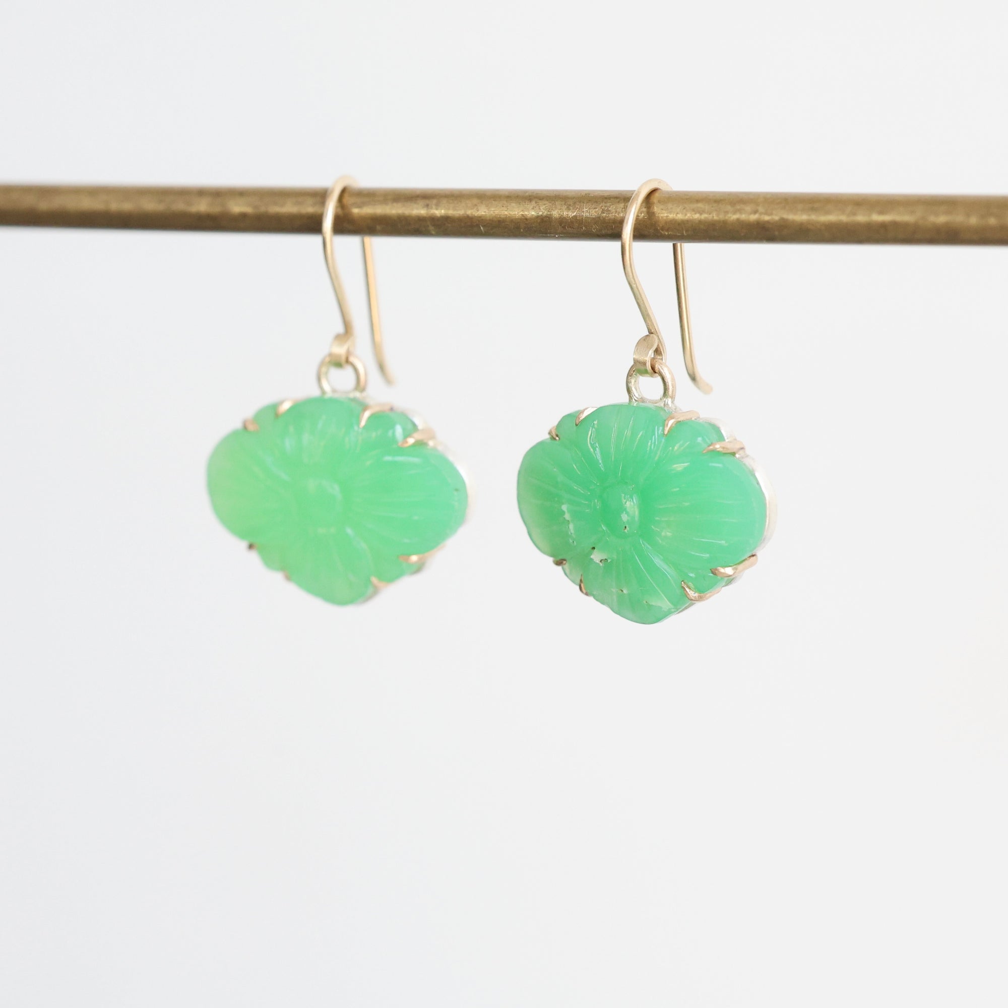 Pair of green earrings on a thin rod against a light gray background