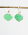 Pair of green earrings on a thin rod against a light gray background