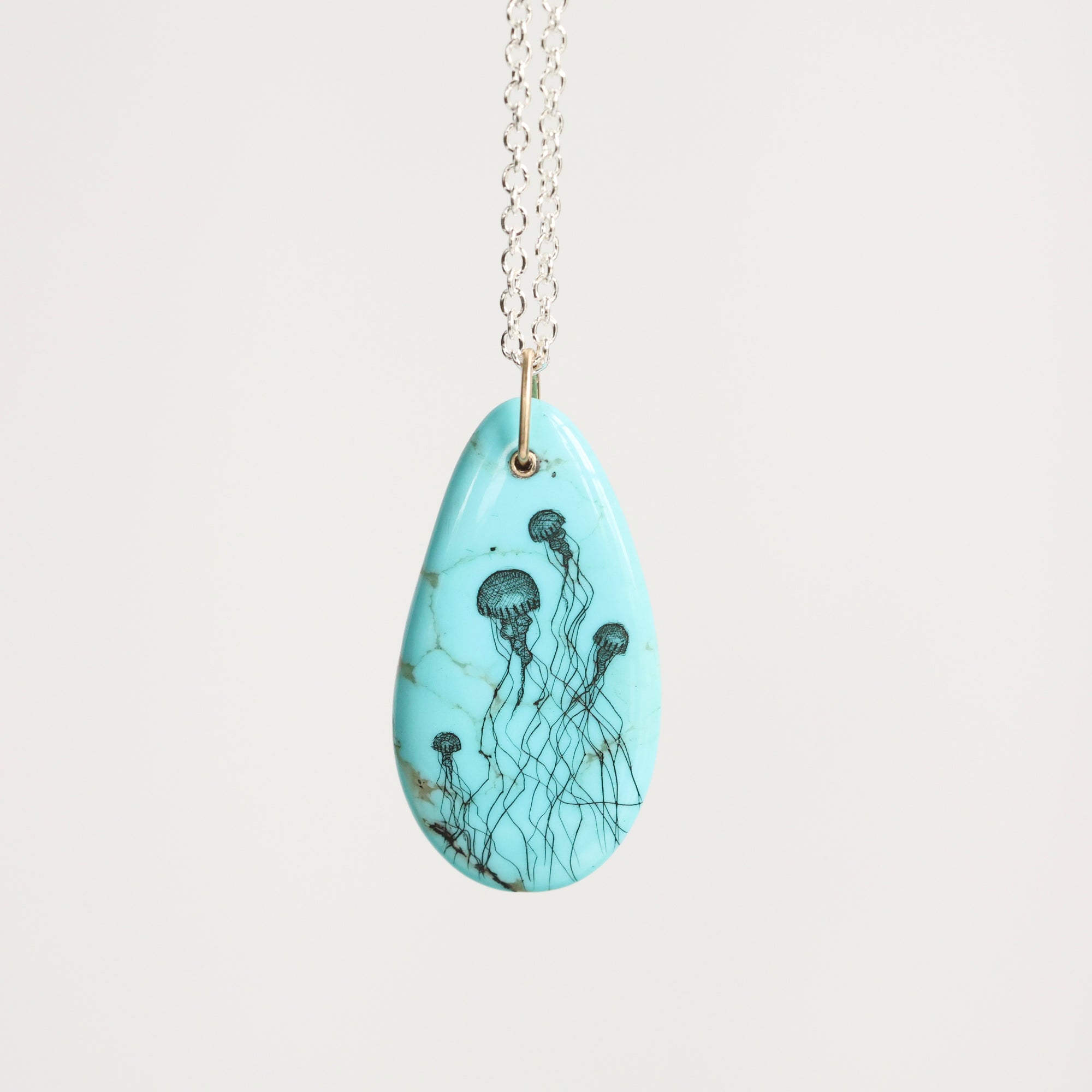 Teardrop-shaped pendant with jellyfish design on a light blue background