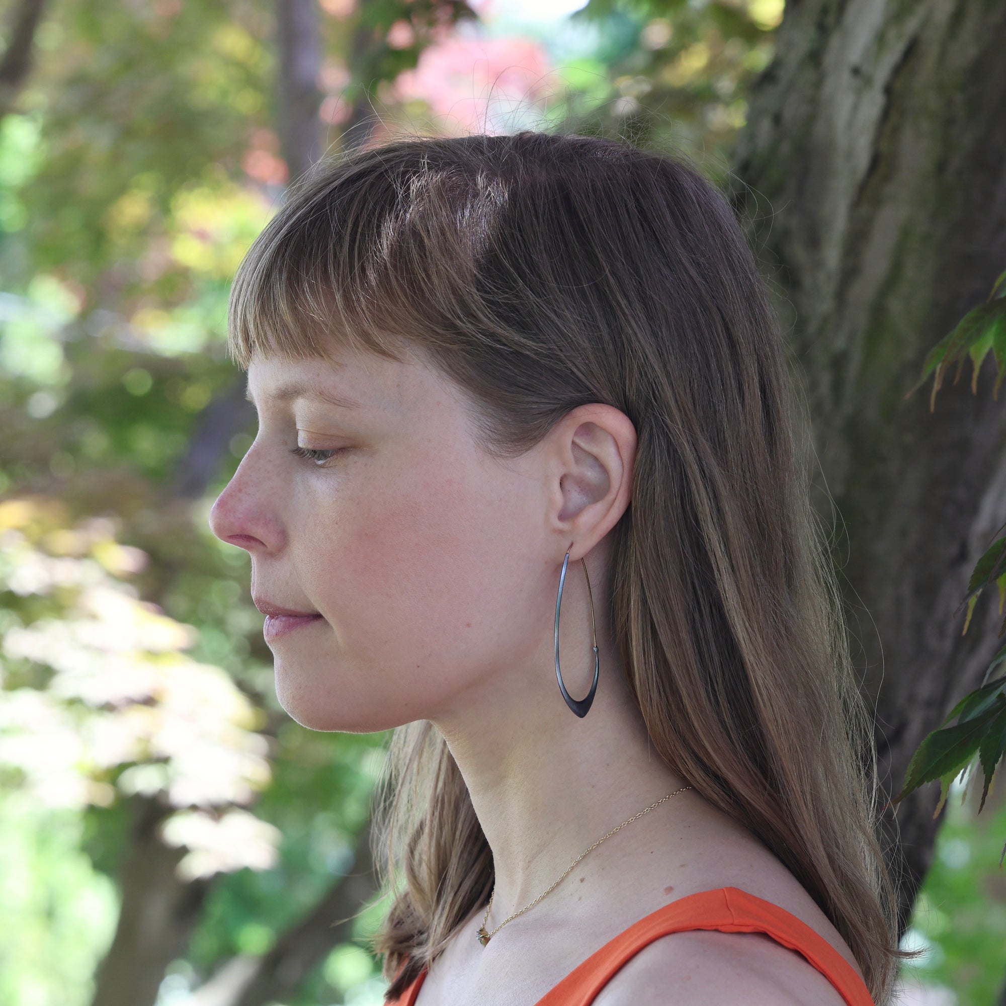 Woman with hoop earrings looking to the side with trees in the background