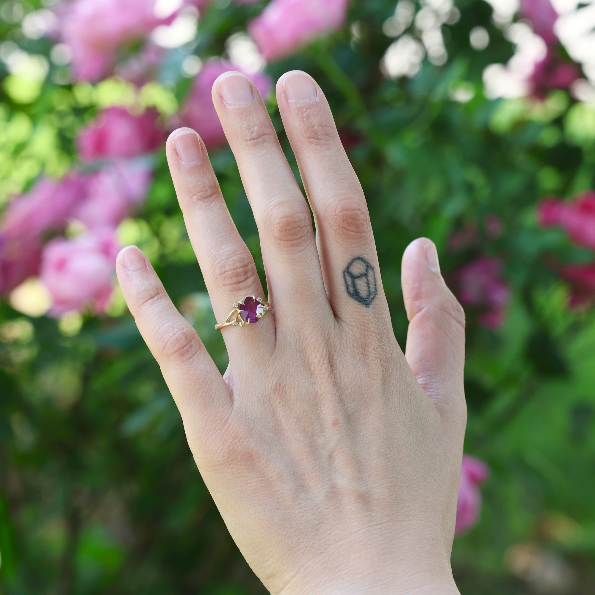 Hand with a ring and tattoo against a blurred floral background