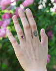 Hand with a ring and tattoo against a blurred floral background