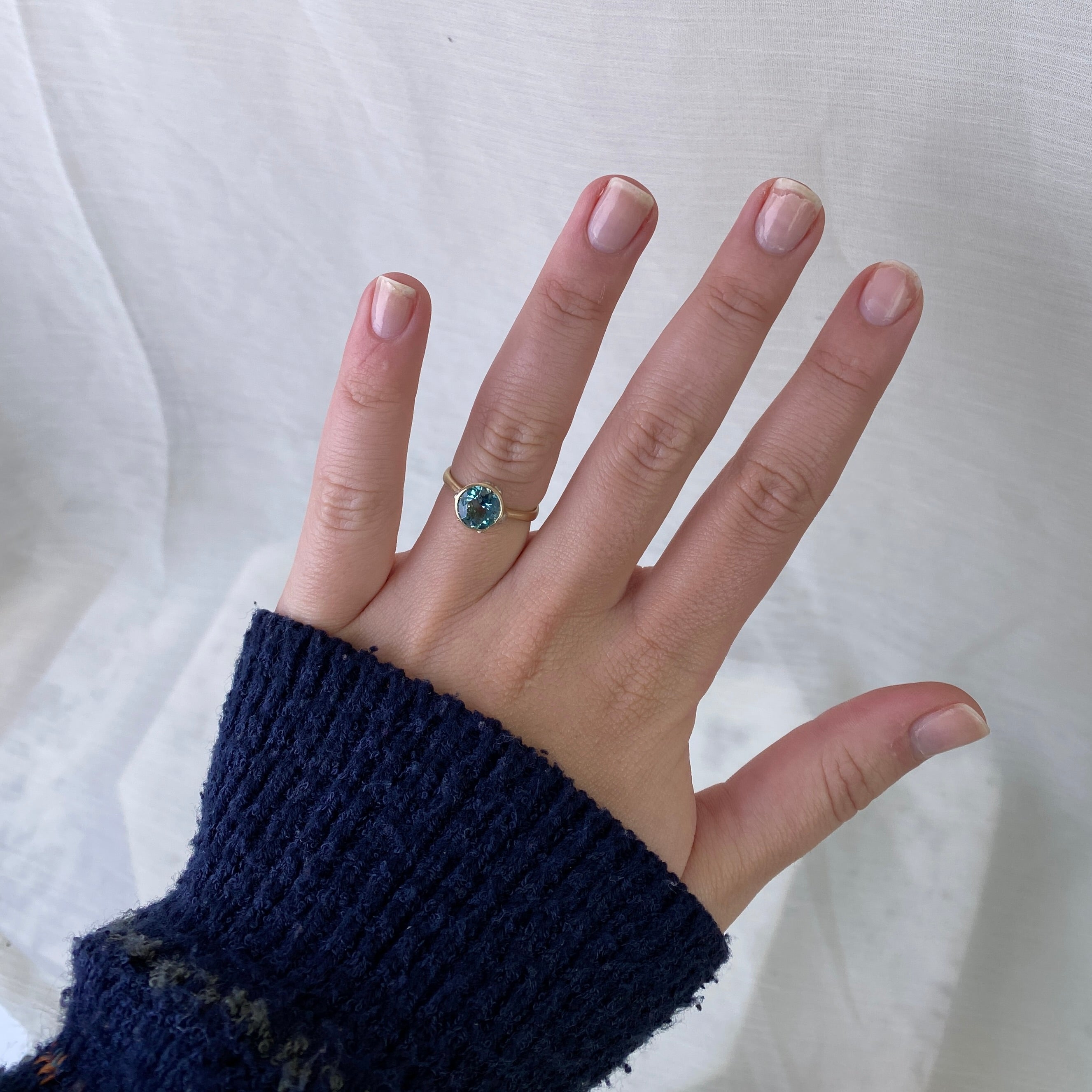 Hand wearing a ring with a blue gemstone against a white background