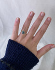 Hand wearing a ring with a blue gemstone against a white background