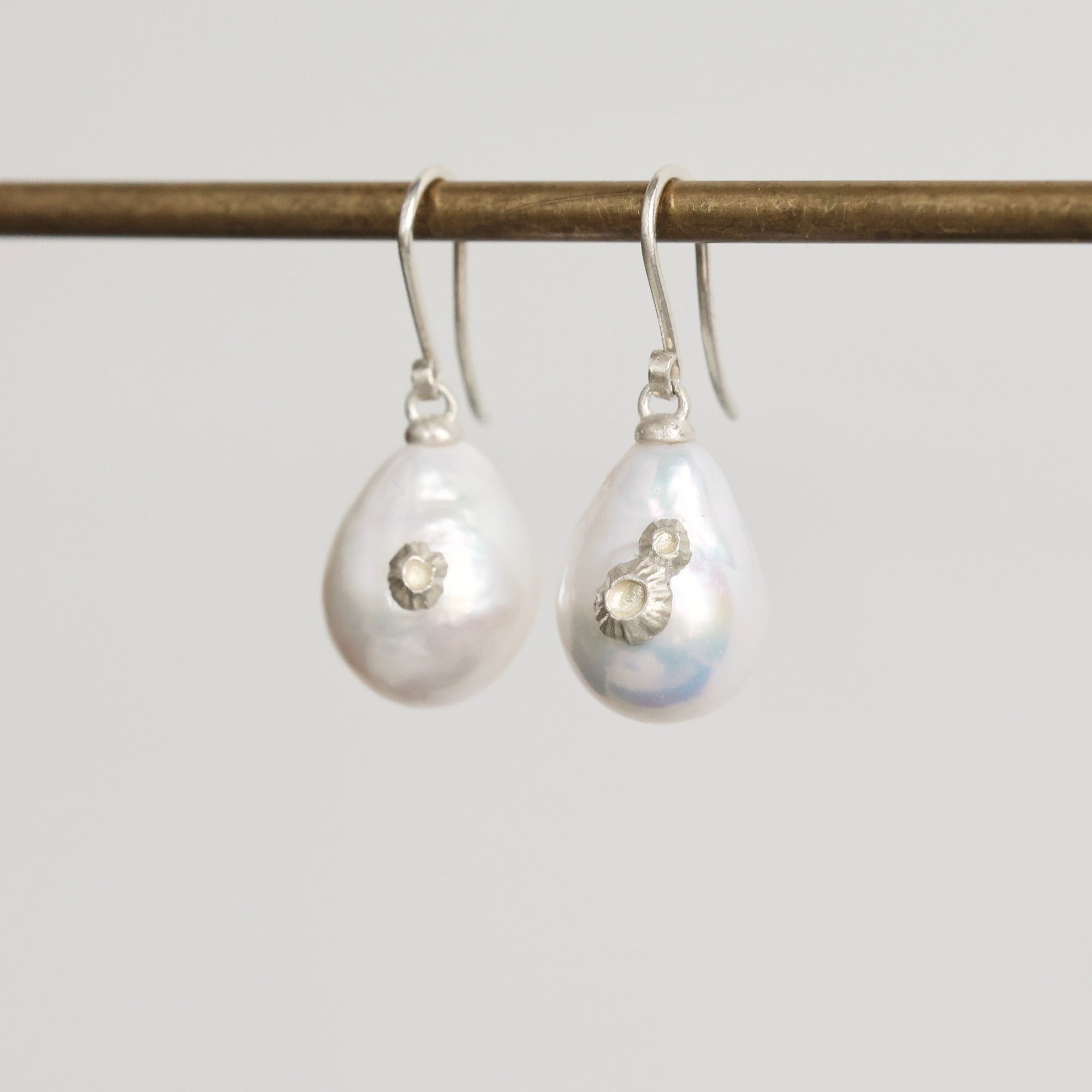Pair of teardrop-shaped pearl earrings with silver hooks on a light gray background