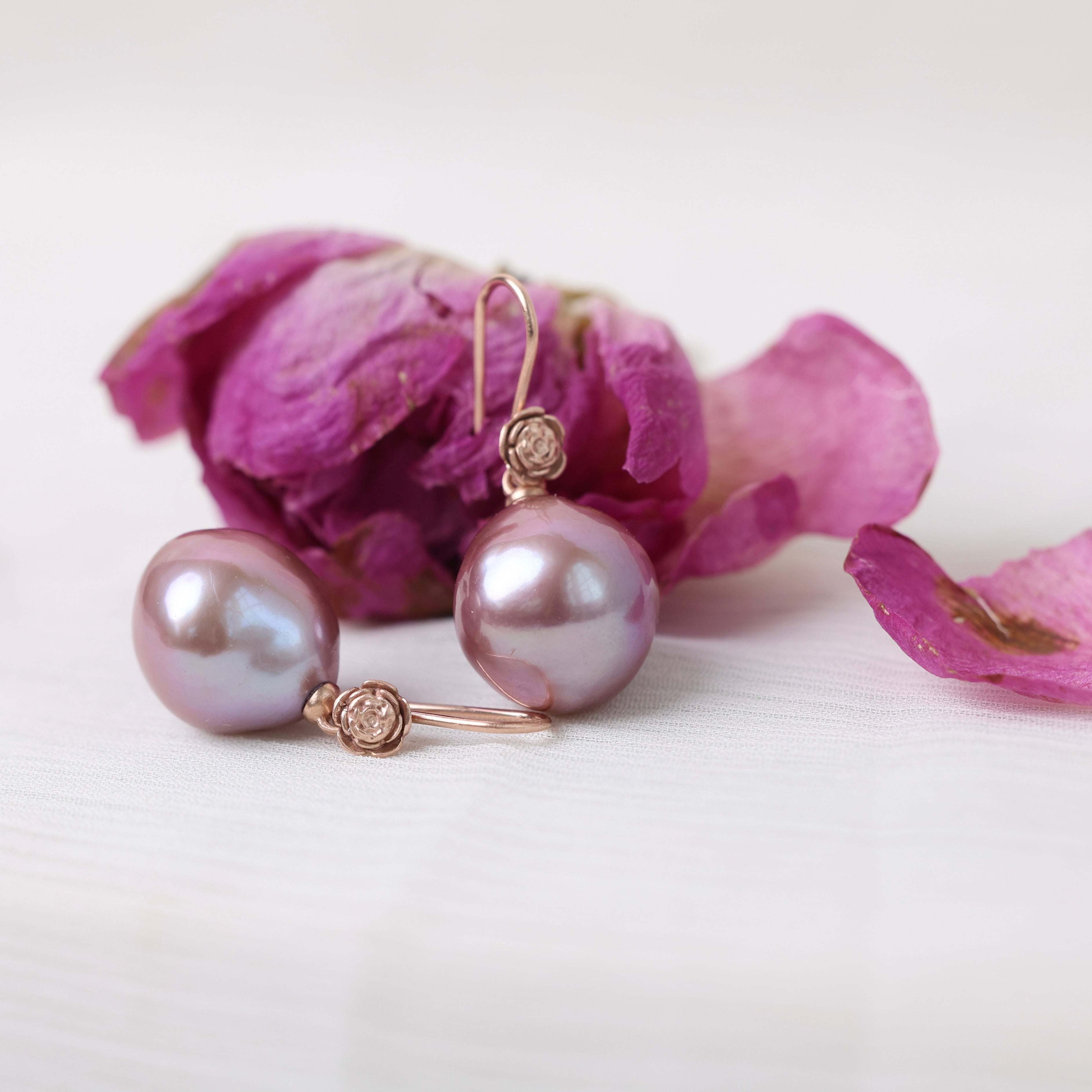 Pearl earrings with gold accents on a white background with pink flowers.