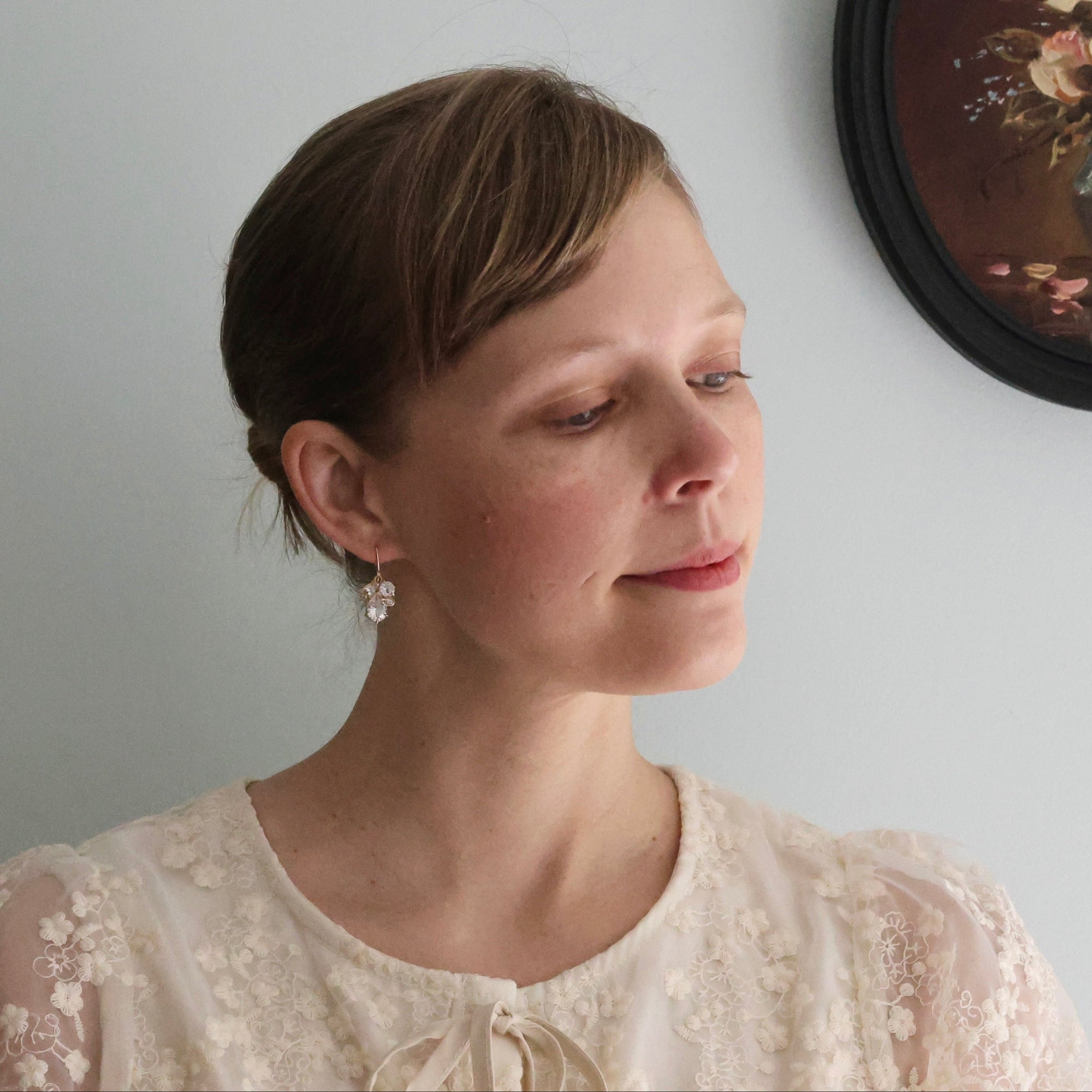 Woman wearing drop herkimer earrings standing next to a flower painting